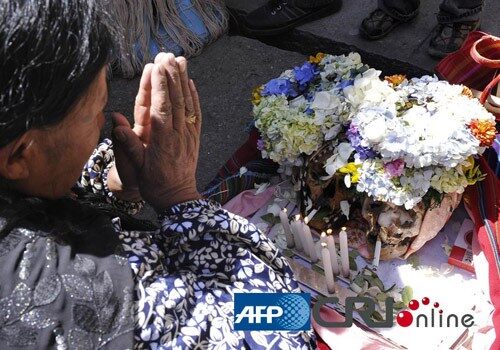 一名老妇人跪在一个头骨前面祈祷。图片来源：(AFP/国际在线)  